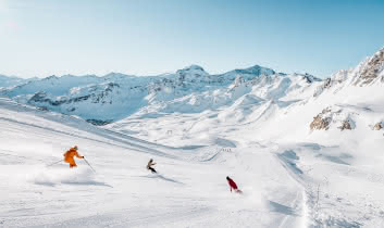 Des skieurs et snowboardeurs dévalent la piste rouge Cyclamen avec vue sur la Grande Motte