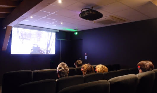 Ecran de cinéma devant lequel sont assis des spectateurs dans des fauteuils