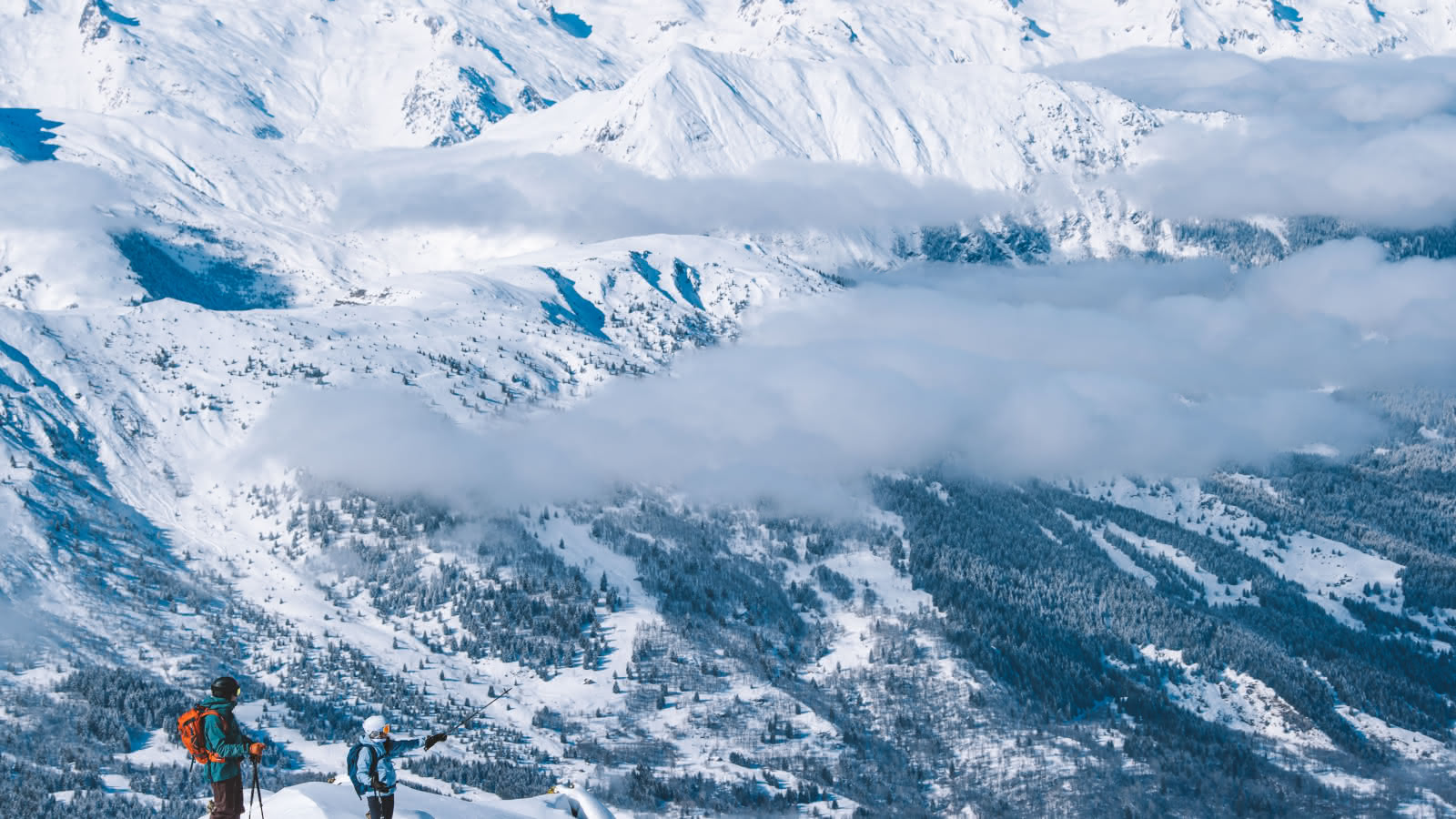 2 skieurs sont arrêtés sur un sommet et pointent un sommet des 3 Vallées.