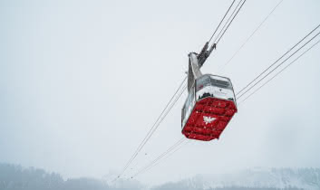 Une vue impressionnant en contre bas d'une cabine du téléphérique du Fornet. Le dessous rouge de la cabine avec son logo blanc ressort dans le paysage blanc de l'hiver.