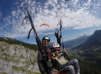child in a paraglider with pilot, blue sky and clouds